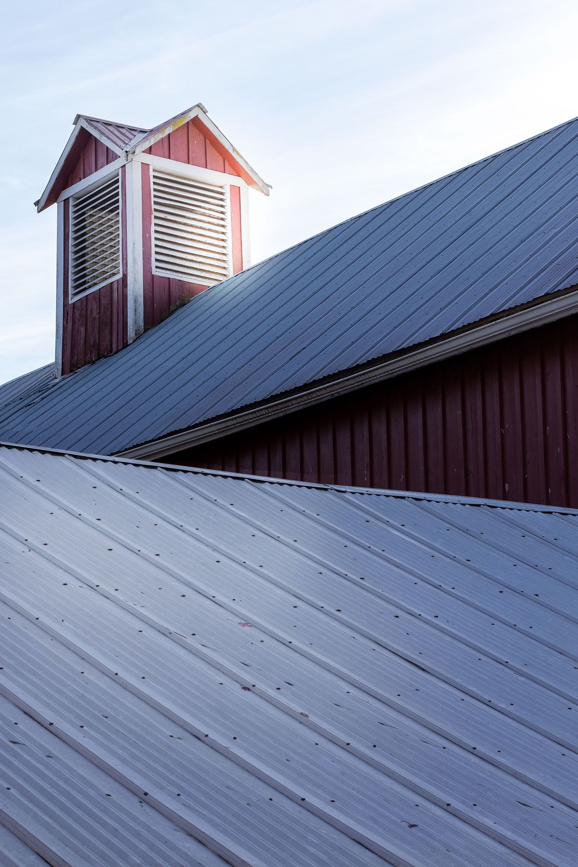 Close-up of a textured metal rooftop featuring a red vent structure, captured at sunset enhancing shadows.