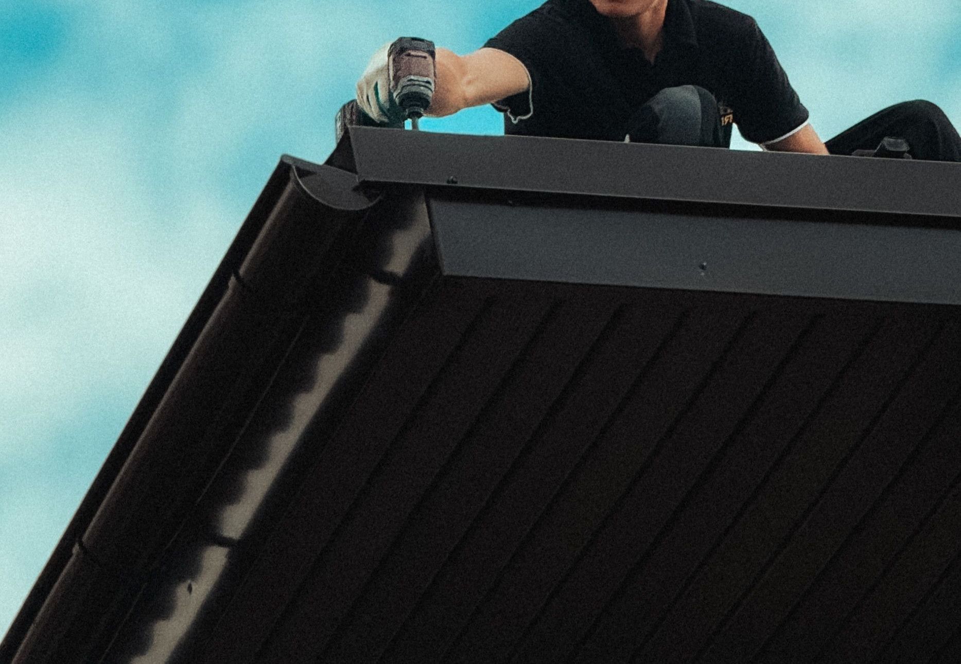 Roofer working diligently on a house roof under a bright blue sky. Professional roofing maintenance in progress.